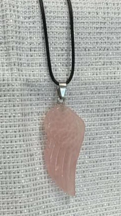 Pink rose quartz angel wing crystal with silver findings and a black cord on a textured surface