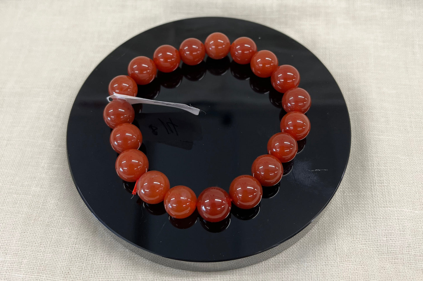 Bracelet of redish/orange semi-translucent beads sits on a black disc on a beige fabric background