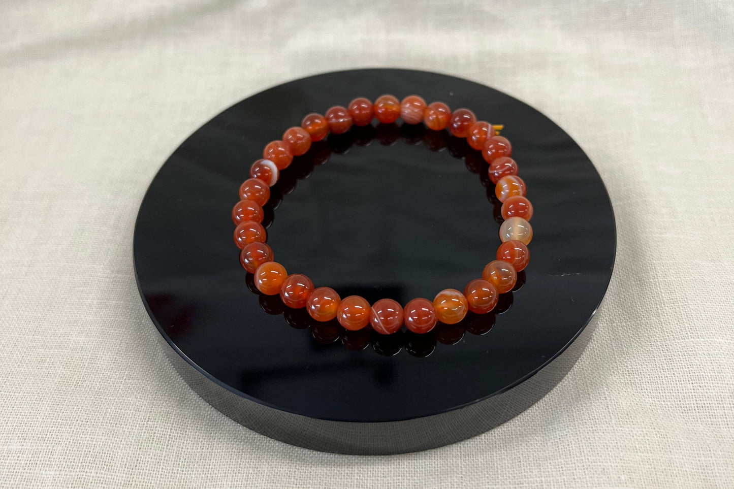 Bracelet with orangeish red marbled beads on a black circular stand against a white fabric background