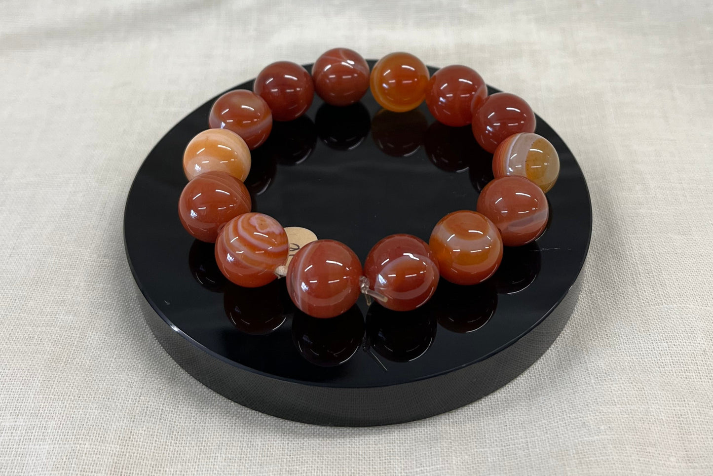 Bracelet of large round polished carnelian stones with marbled red/orange/cream patterning on a black stand against a beige fabric background