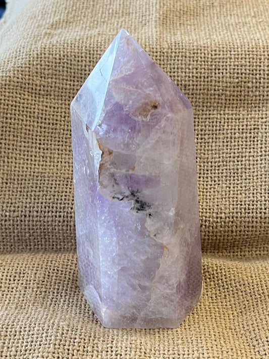 Purple amethyst crystal is shown in a setting with more light, showing areas of brown coloration and black inclusion on the mainly purple stone.