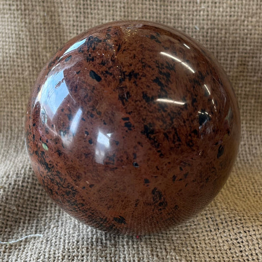 Red polished stone with black mottled inclusions on a textured beige fabric