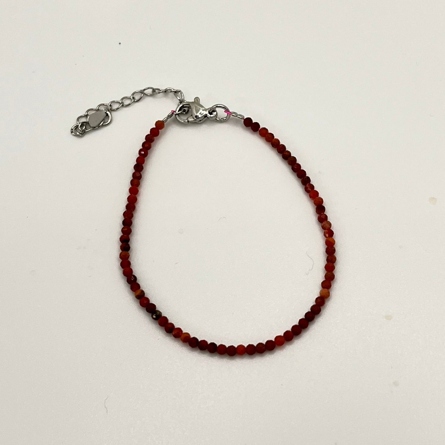 Bracelet of small faceted red and black marbled beads with a silver colored chain and findings.