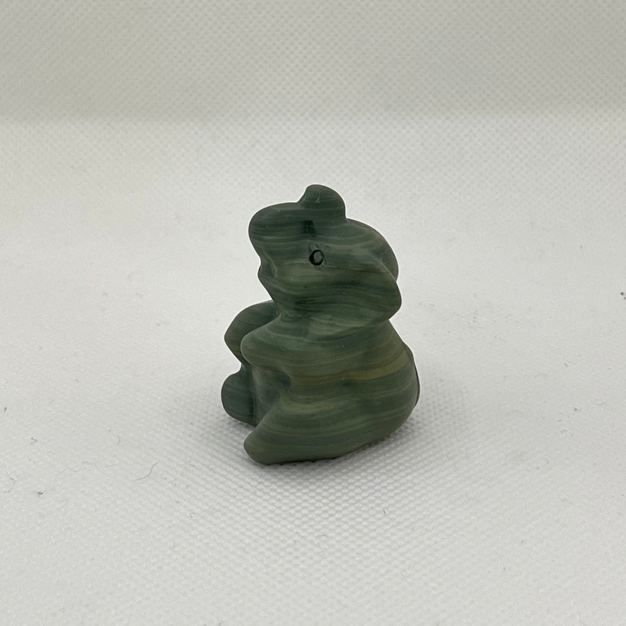 Green statue of a jade elephant on a white surface from the side view.