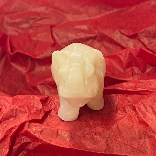 A small carved pale stone figurine of an elephant, resting on crumpled red tissue paper.