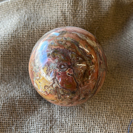 Round, brownish mottled stone on a textured beige fabric background