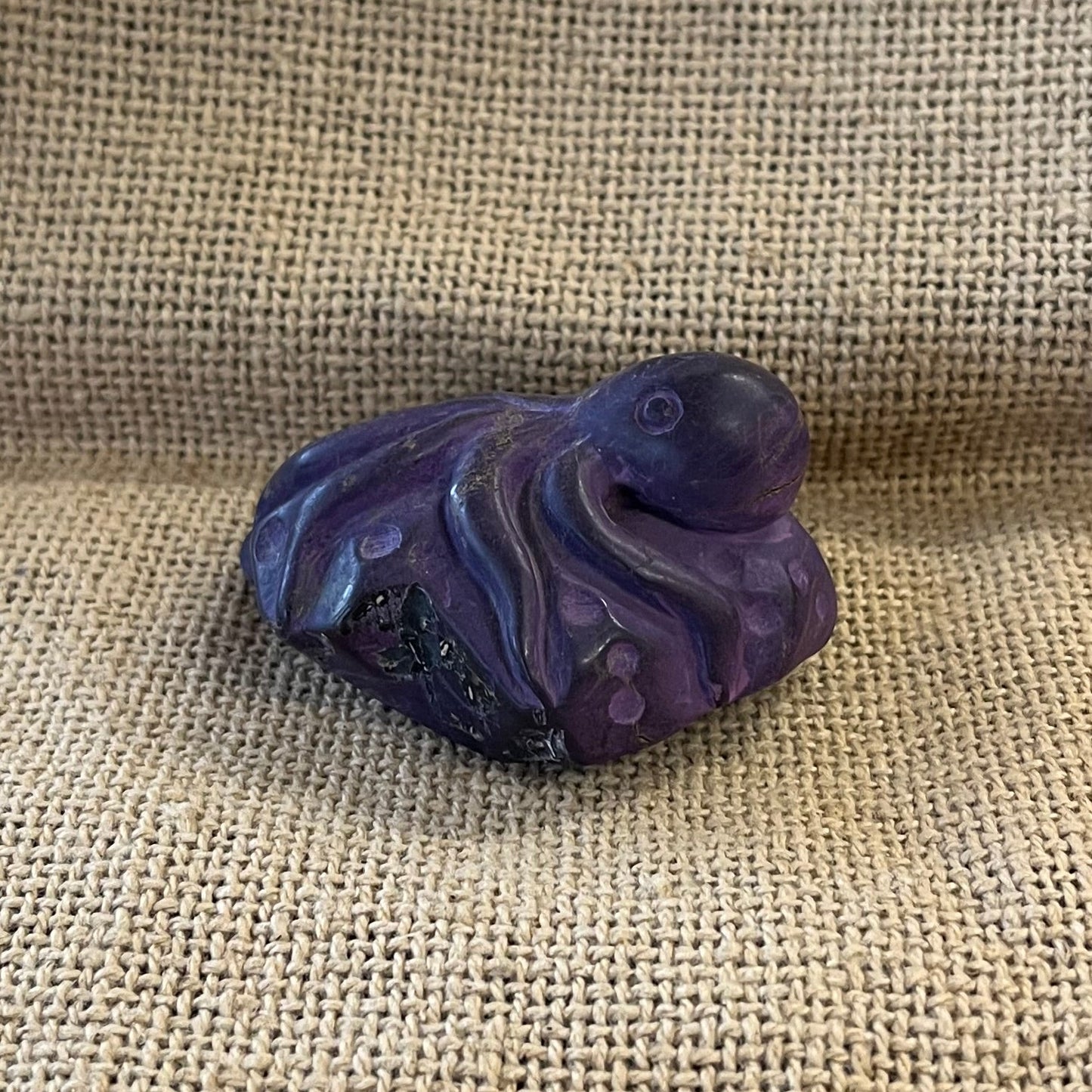 Purple sugilite carving of an octopus laying on a stone.