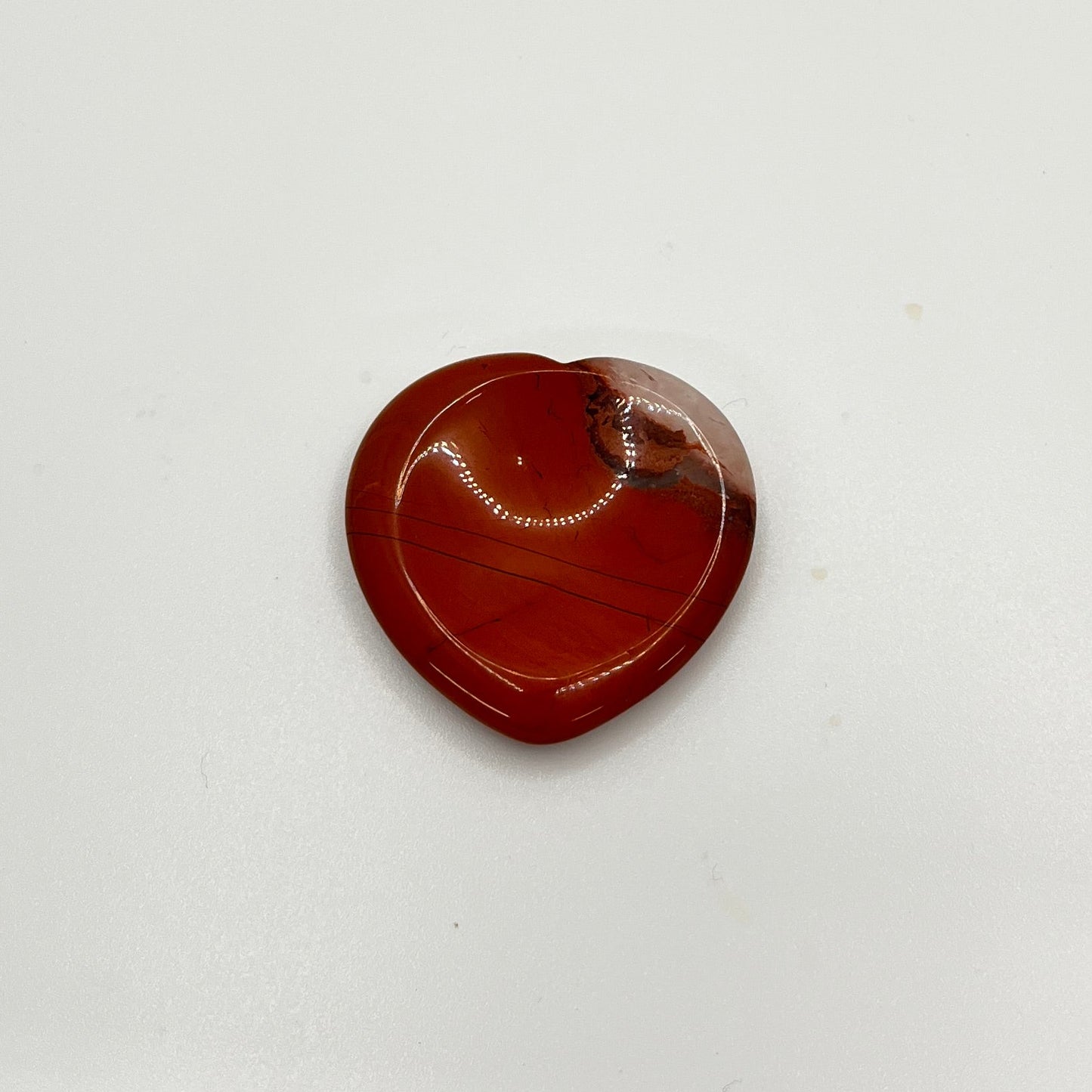 A red stone with white in the corner is in the shape of a heart, with a circular indented area in the middle to rub a thumb on.