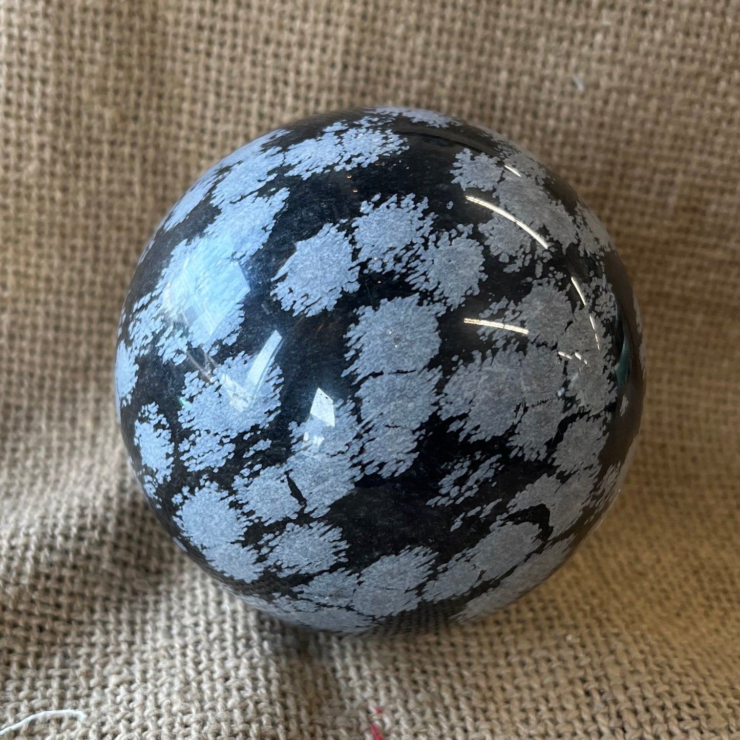 Black sphere with white snowflake pattern on a textured fabric background