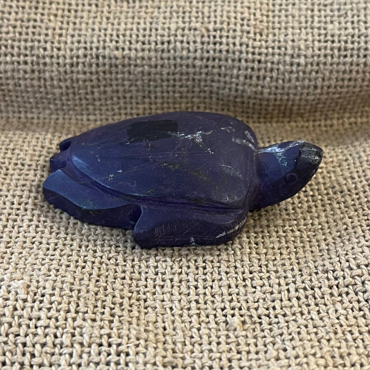 Decorative dark purple and white sea turtle figurine on a textured fabric surface