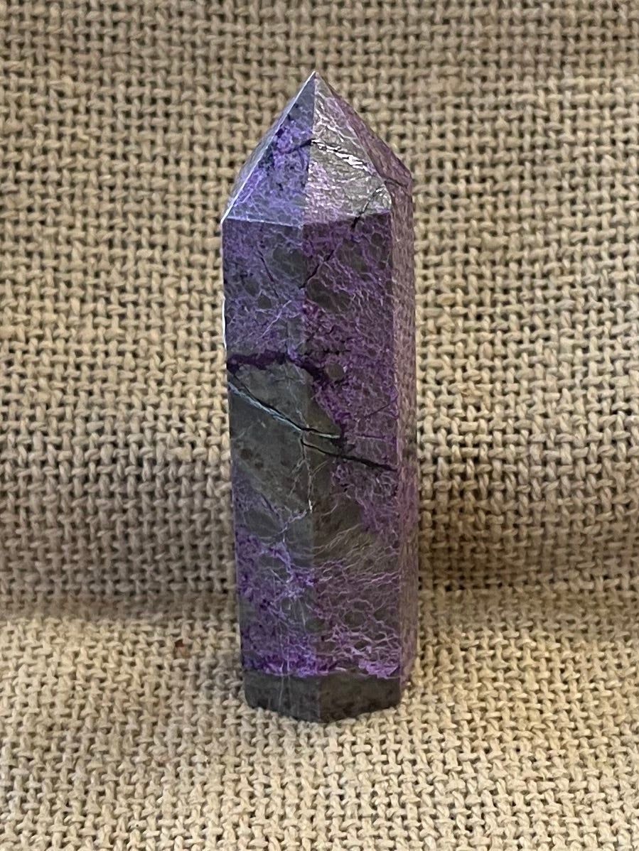 Sugilite crystal on a burlap bag with a blurred background.