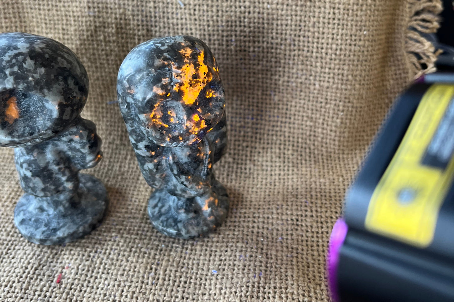 Gray and black patterned stone Jack and Sally statues on a tan textured background. A black light is shining on Sally and parts of the stone are glowing a yellow-orange color.