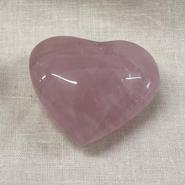 A shiny pink semi-transparent heart-shaped stone on a textured beige fabric background