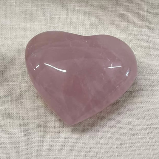 A shiny pink semi-transparent heart-shaped stone on a textured beige fabric background