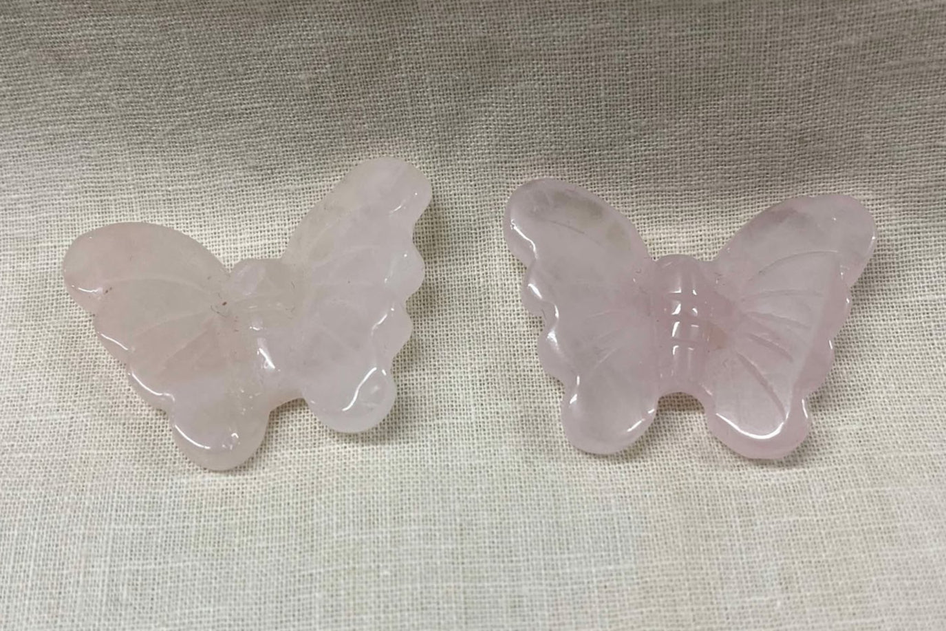 Two pink butterfly-shaped light pink semi-transparent crystals on a textured beige surface