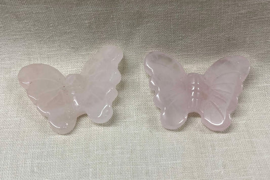 Two pink butterfly-shaped light pink semi-transparent crystals on a textured beige surface