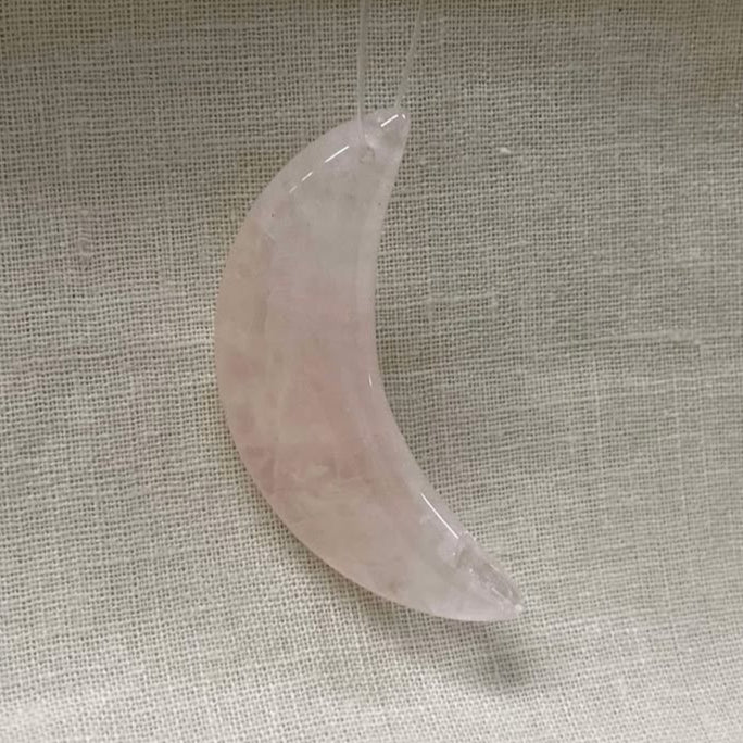 Pink crescent moon-shaped crystal on a textured beige fabric background