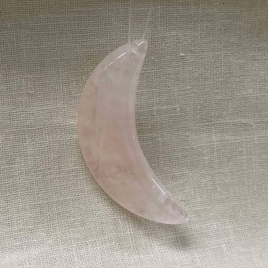 Pink crescent moon-shaped crystal on a textured beige fabric background