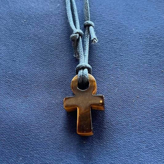Light and dark brown ankh pendant hanging from a blue cord on a blue fabric background
