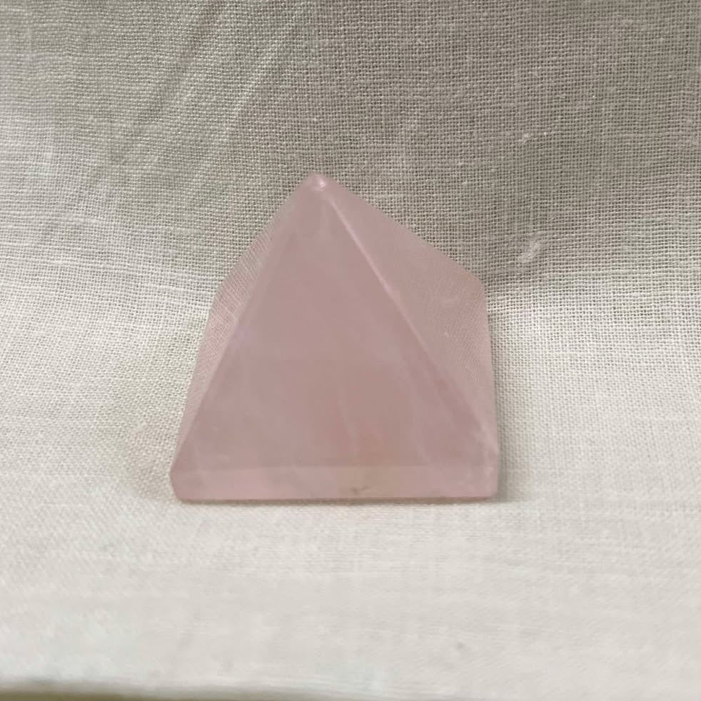 Light pink semi-transluscent crystal in a pyramid shape against a cream background.