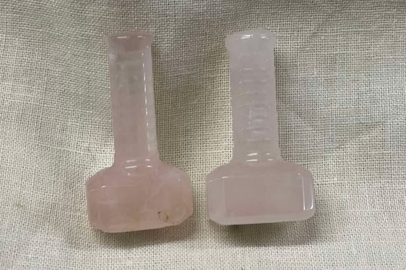 Two small pale pink crystals shaped like Thor's hammer on a textured beige background