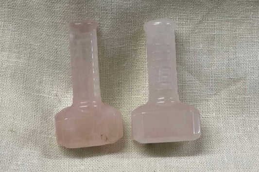 Two small pale pink crystals shaped like Thor's hammer on a textured beige background