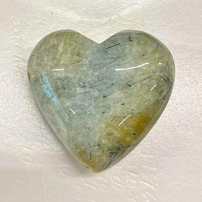 Heart-shaped prehnite stone on a white card with a blurred background