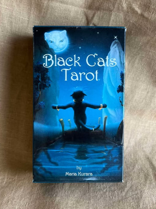 Black Cats Tarot card box features a black cat standing at the end of a dock on a moonlit night, wearing gold bracelets, a gold necklace, and a gold tail ring.