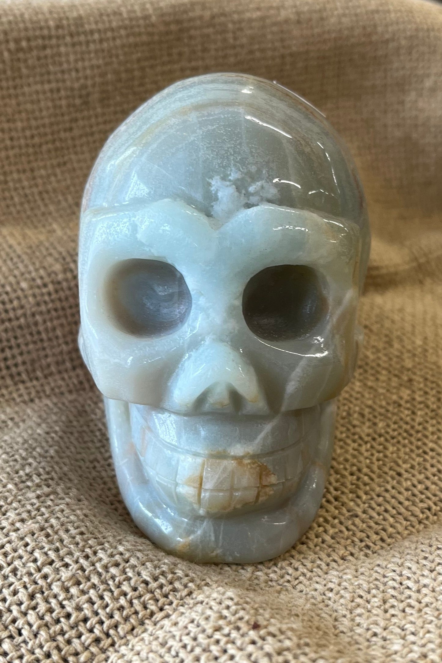 Pale aqua crystal skull on a textured fabric background. Hues of brown are present in the stone as well.