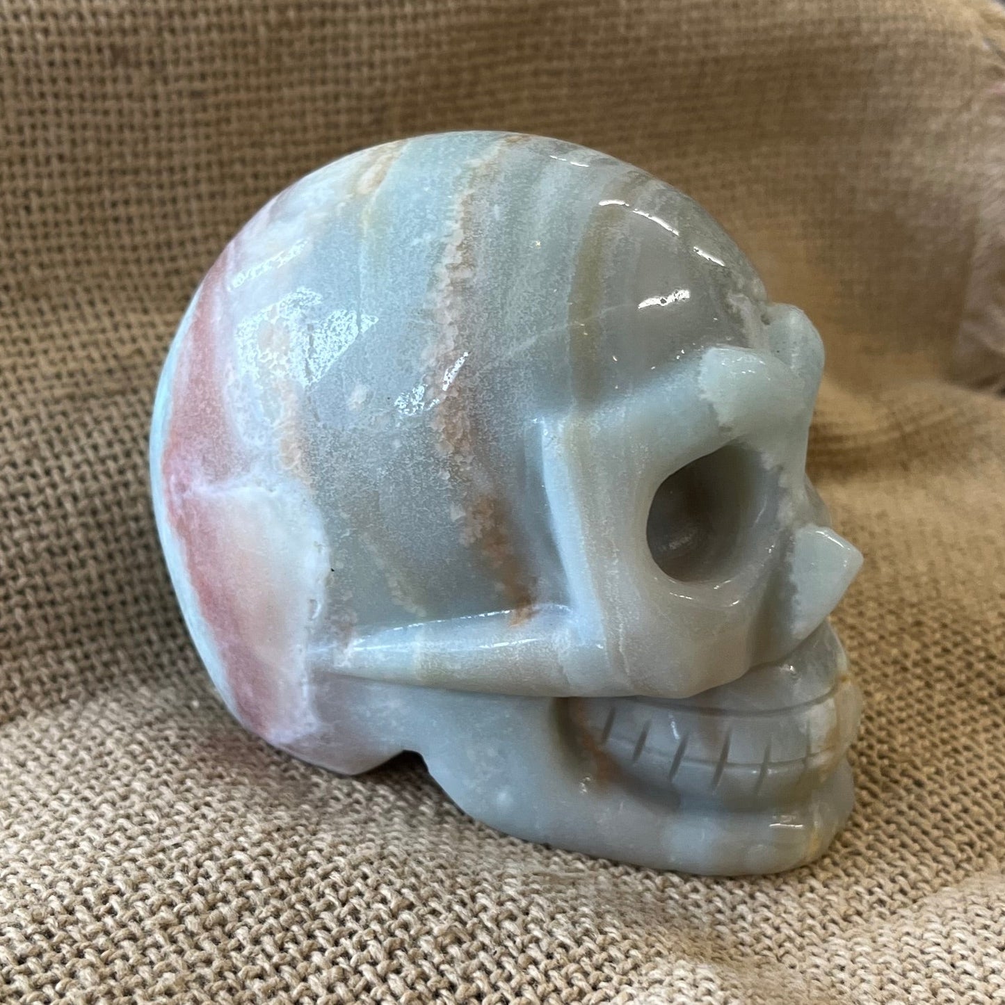 Pale aqua crystal skull on a textured fabric background. Layers of tans and browns brown are present in the stone as well.