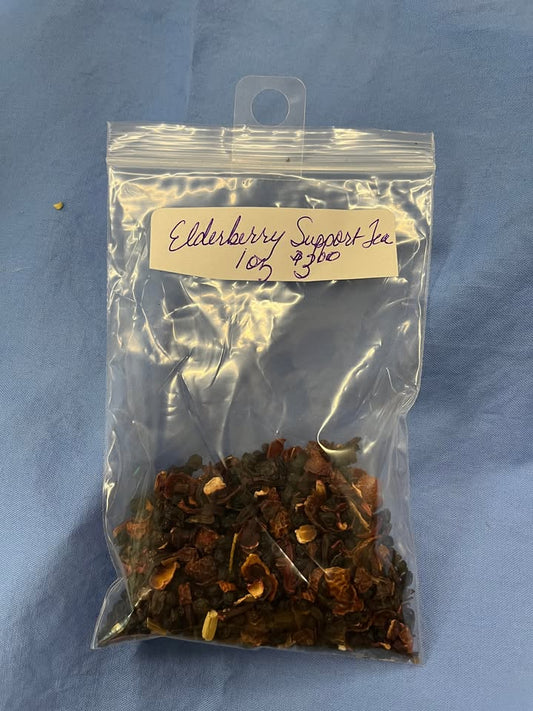 Blend of red dried rose hips, black dried elderberries, dark red dried flowers, and other dried herbs in a clear plastic bag, with a label saying "Elderberry Support Tea, 1 oz for $3.00"  