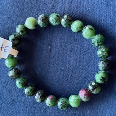 Green beaded bracelet, with black and purple in the green beads, with a tag on a blue fabric background