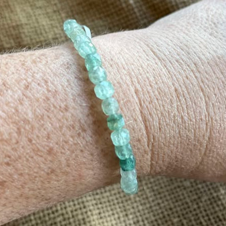 Green faceted bead bracelet on a wrist with a textured beige background