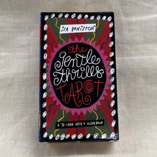 Box of 'The Gentle Thrills Tarot' on a textured gray background features cursive writing, pink, red, green, yellow, white, and blue artwork in a whimsical style.