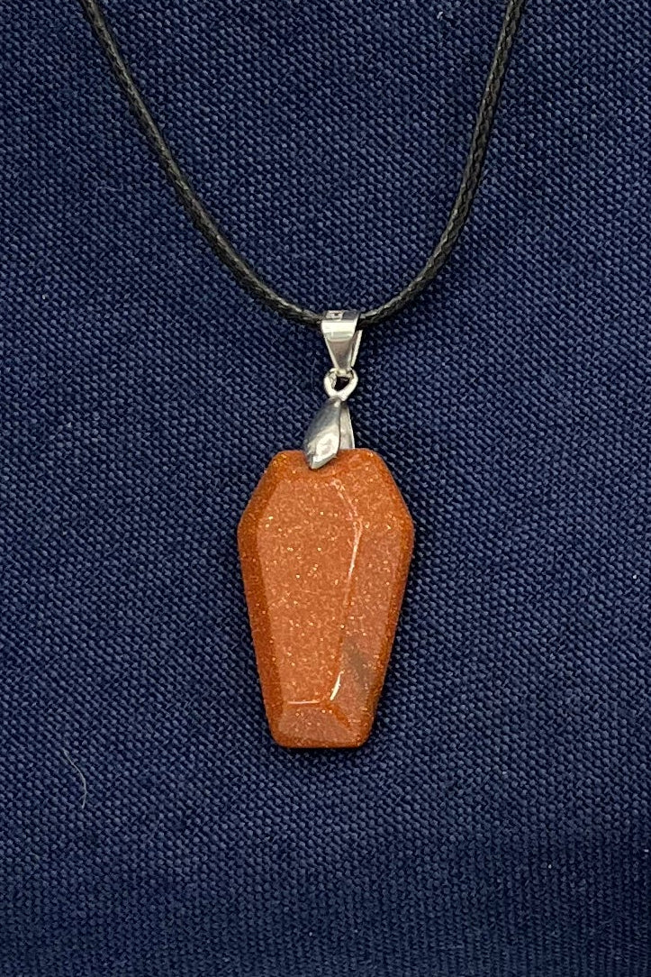 Necklace with an orange-red sparkling coffin pendant with a silver finding and black cord on a blue fabric background 