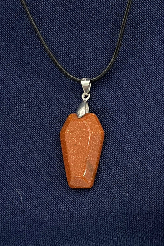 Necklace with an orange-red sparkling coffin pendant with a silver finding and black cord on a blue fabric background 