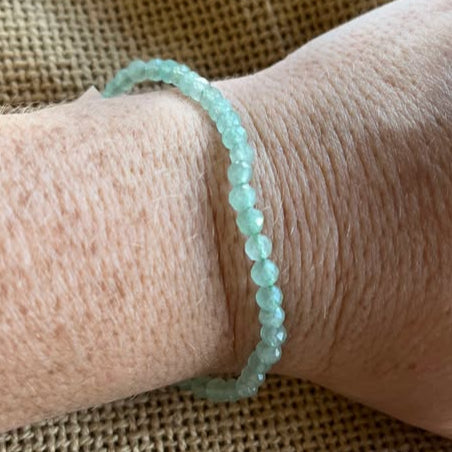 Hand wearing a green faceted bead bracelet on a textured beige fabric background