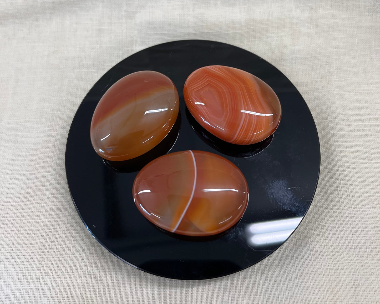 Three carnelian oval stones on a black circular plate with a beige fabric background