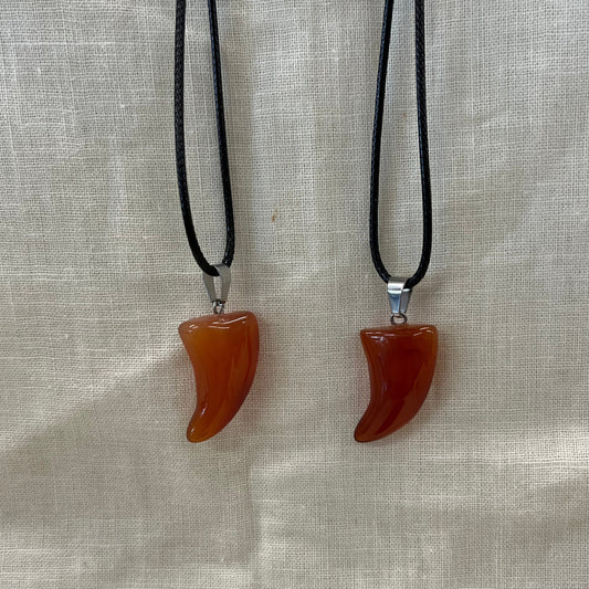 Two necklaces with semi-translucent orange-red pendants in the shape of teeth on a light fabric background
