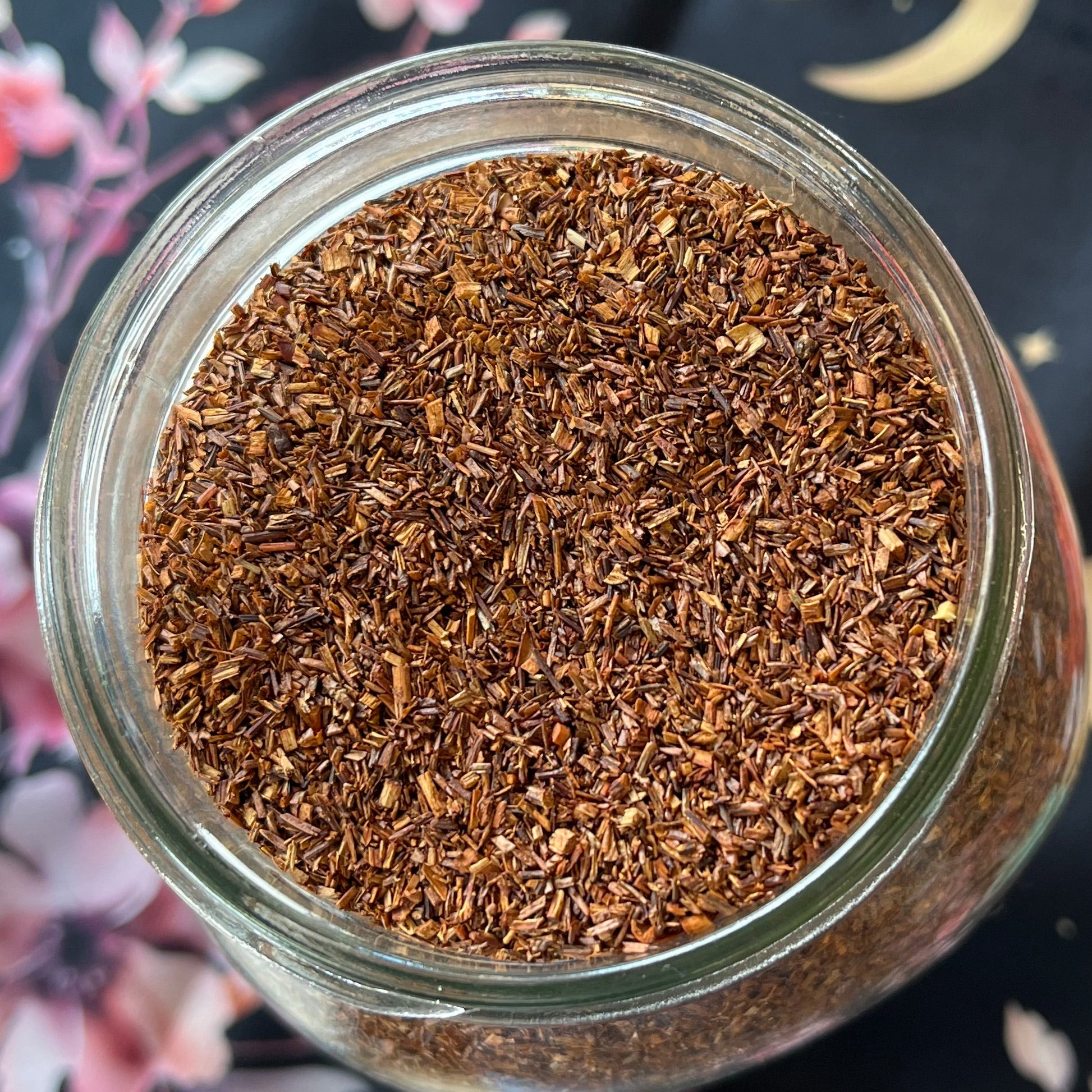 Glass jar filled with brown ground tea leaves on a decorative cloth background