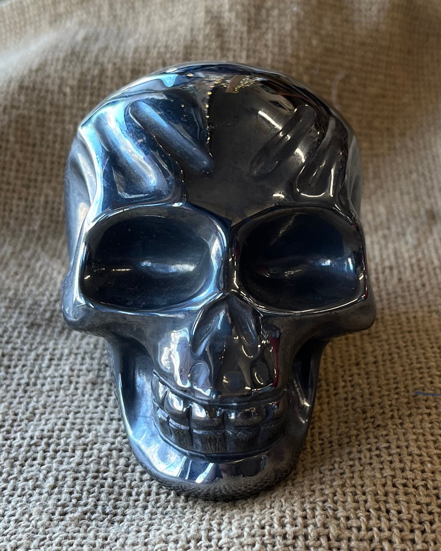 Metallic dark silver-colored skull on a textured beige surface