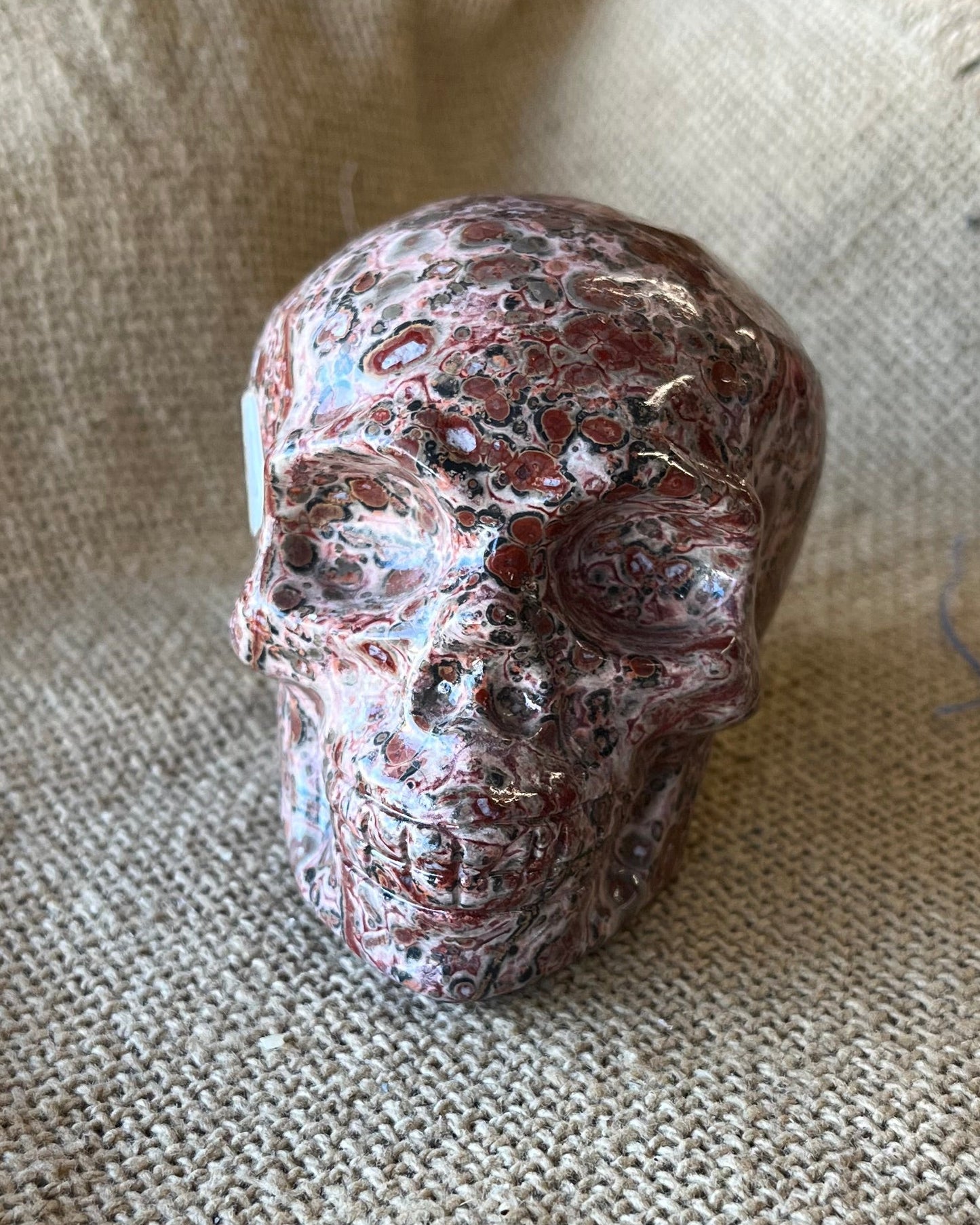 Brown, tan, and red mottled stone skull on a textured beige surface 