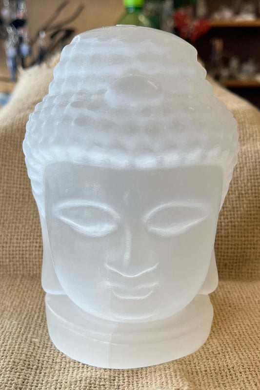 A white-ish opaque buddha head figure seems to glow in the light as it sits on a tan textured background.