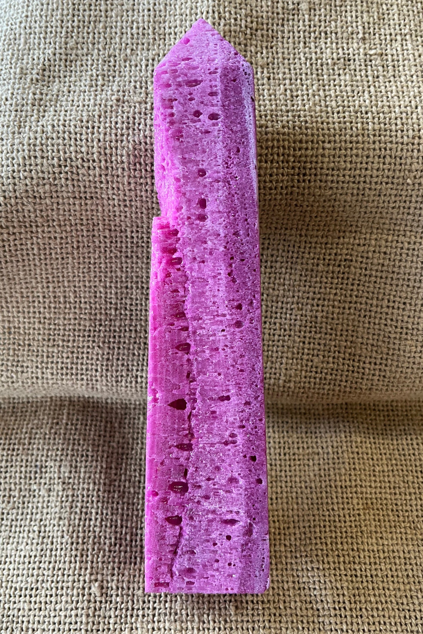 Purple raw crystal on a textured beige fabric background. The stone is uneven.