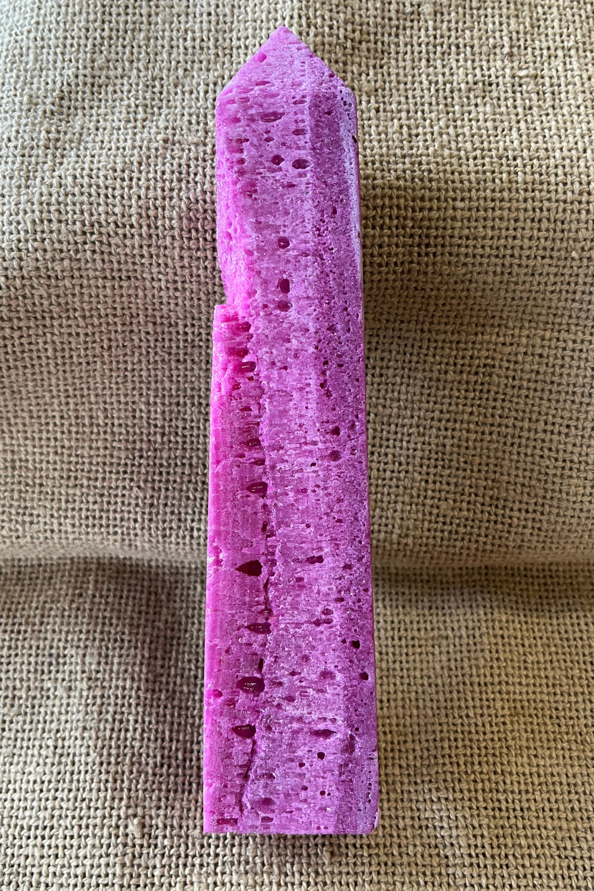 Purple raw crystal on a textured beige fabric background. The stone is uneven.