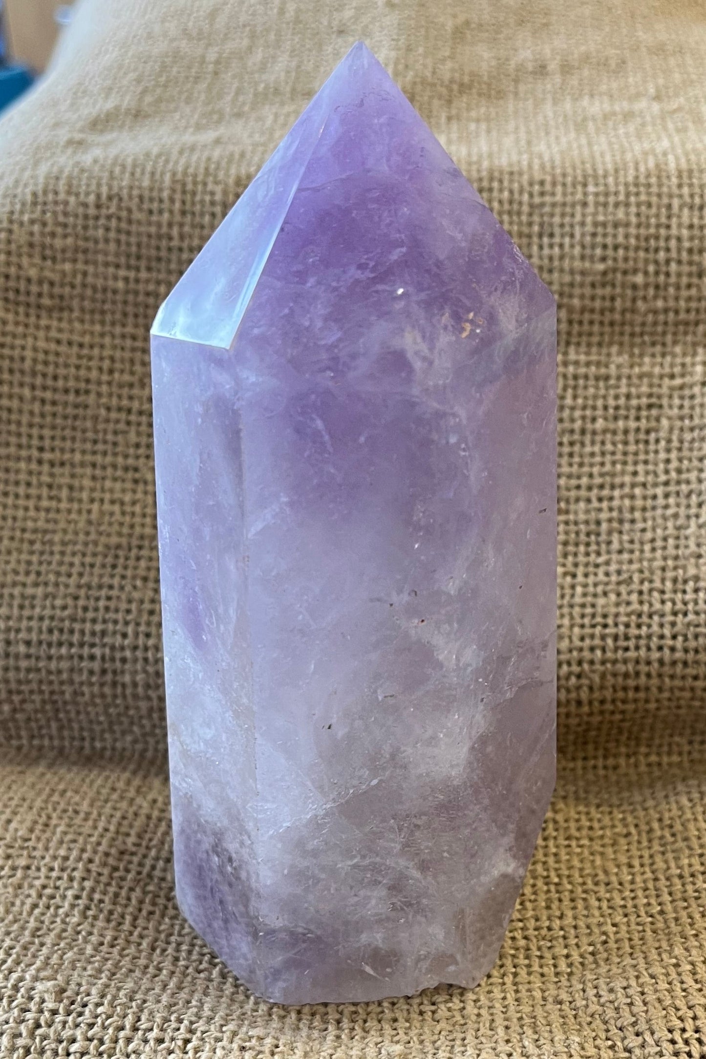 Purple crystal in the shape of a thick tower, on a textured fabric background.  