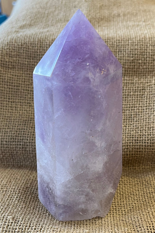 Purple crystal in the shape of a thick tower, on a textured fabric background.  