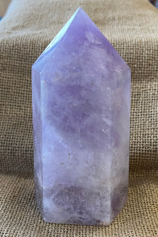 Purple crystal in the shape of a thick tower, on a textured fabric background.
