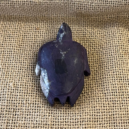 Decorative dark purple and white sea turtle figurine on a textured fabric surface