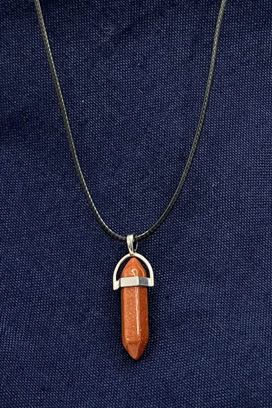 An orange-red sparkling double-pointed gem in a metal finding on a black corded necklace sits on blue fabric